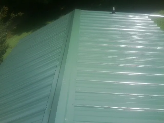New green metal panels meeting at the ridge of a roof — Flat Roof Repair work by our crew in Fort Myers