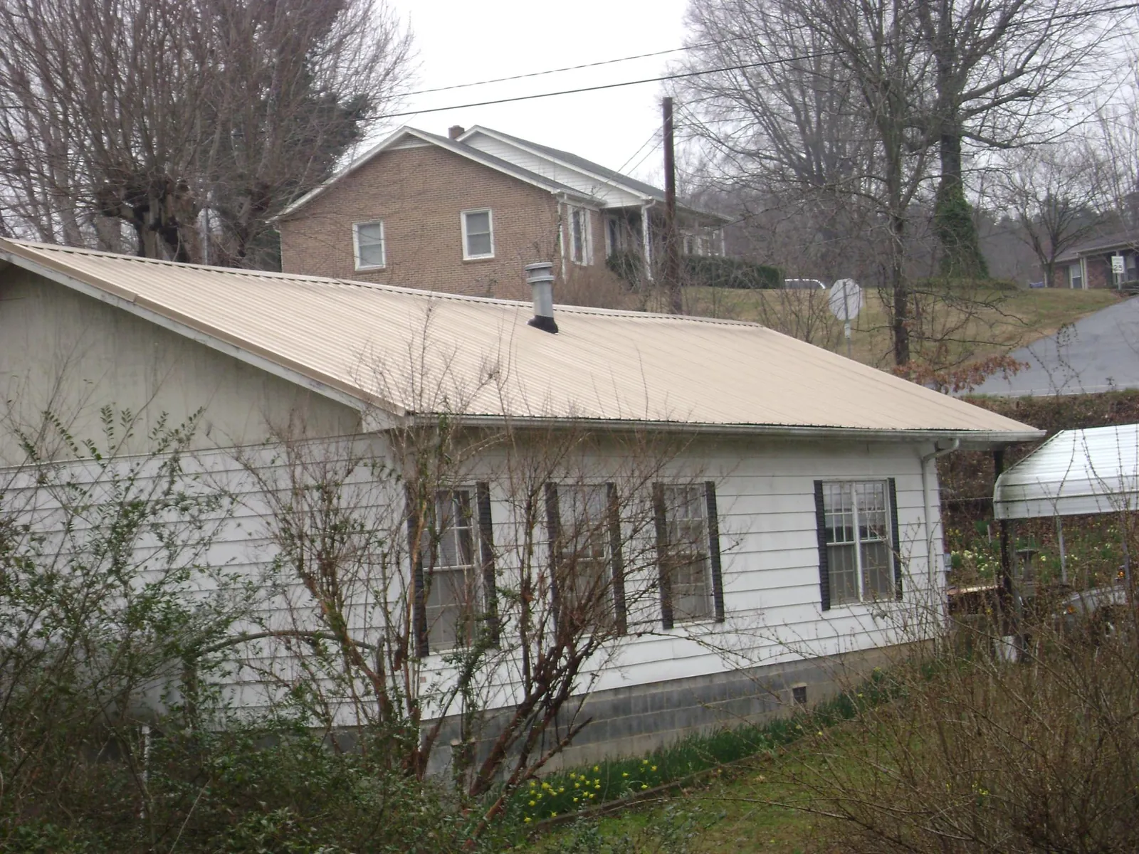 Tan metal roof on a white sided house set into a hillside — Commercial Roofing by Roofing Brothers in Fort Myers